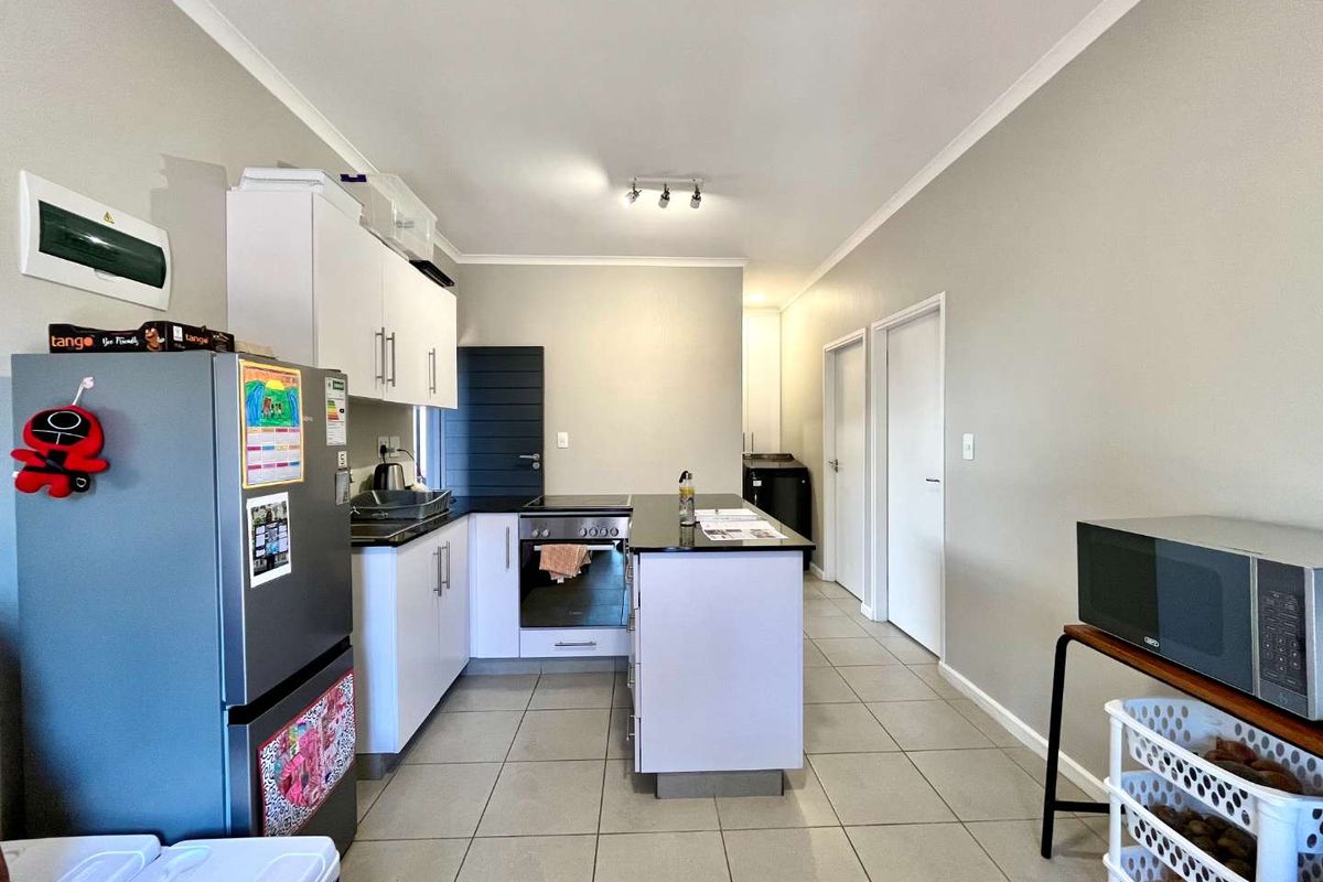 Modern kitchen featuring white cabinetry, dark stone countertops, integrated oven and hob, and neutral tiled flooring in an open-plan layout.