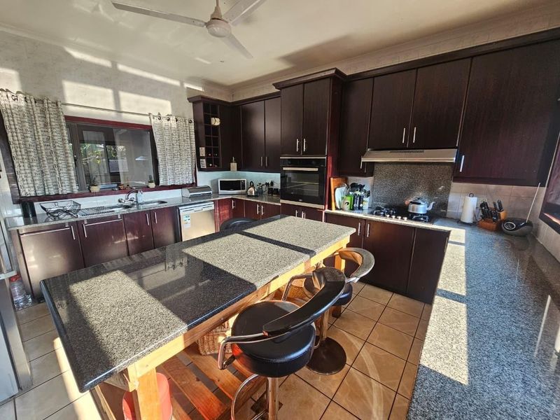 Spacious kitchen featuring dark wood cabinetry, granite countertops, a central island, built-in oven, hob, and tiled flooring.
