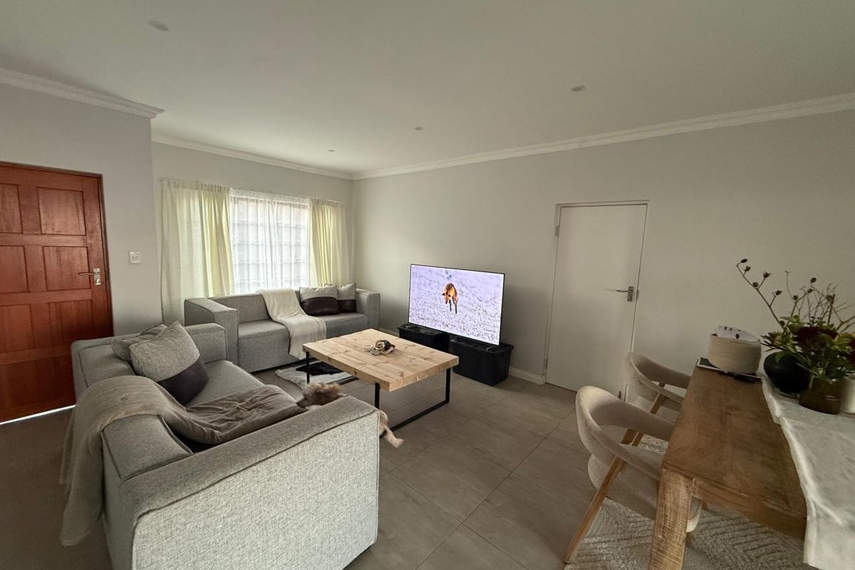 An open-plan living and dining area featuring neutral tiled flooring, recessed ceiling lighting, and a solid timber entrance door.