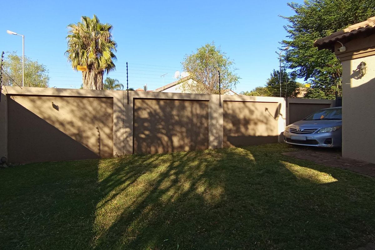 A private rear garden area featuring a well-maintained lawn, perimeter boundary wall with integrated electric fencing, and paved access.