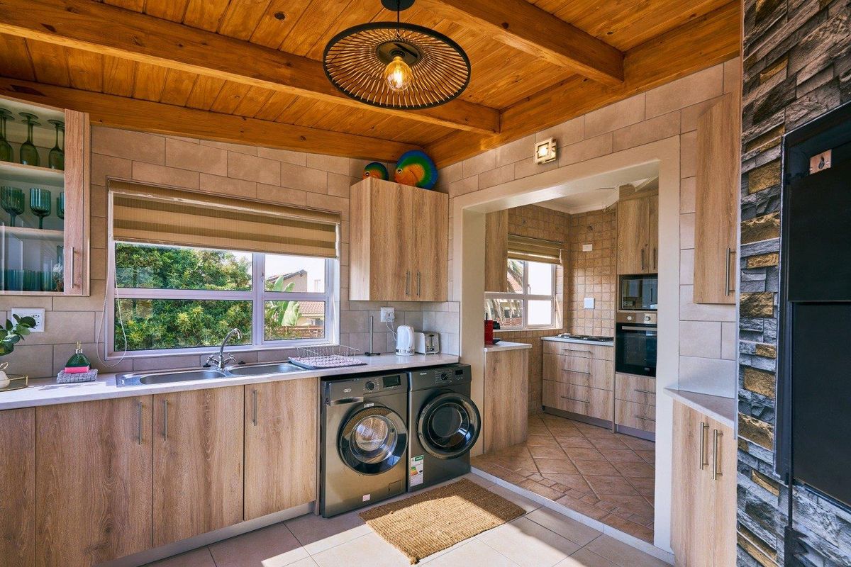 A functional kitchen and laundry area featuring wood-look cabinetry, tiled splashbacks, exposed timber ceiling beams, and integrated appliances.
