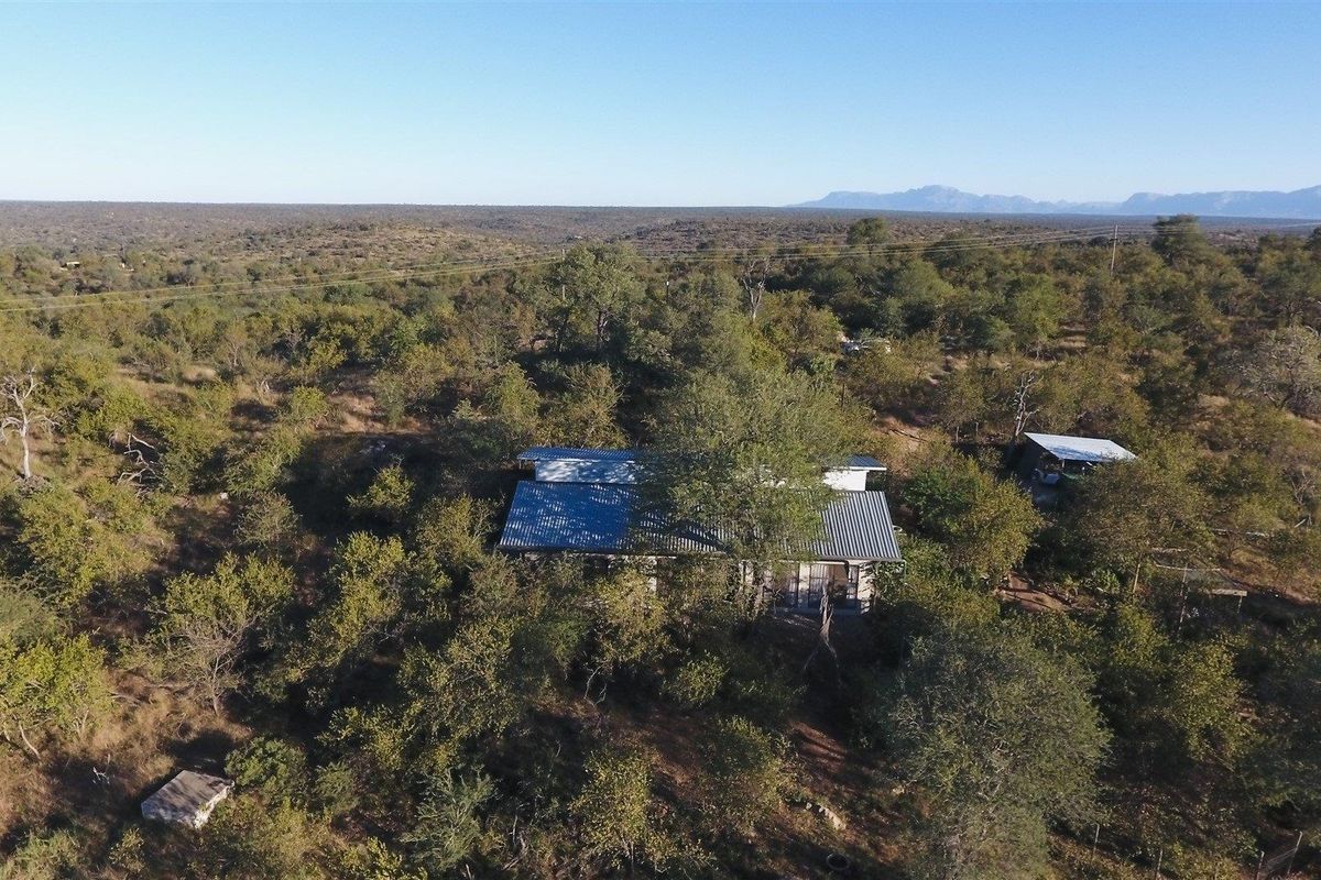 Aerial view of a property nestled within a dense, natural bushveld landscape, featuring a structure with a corrugated metal roof.