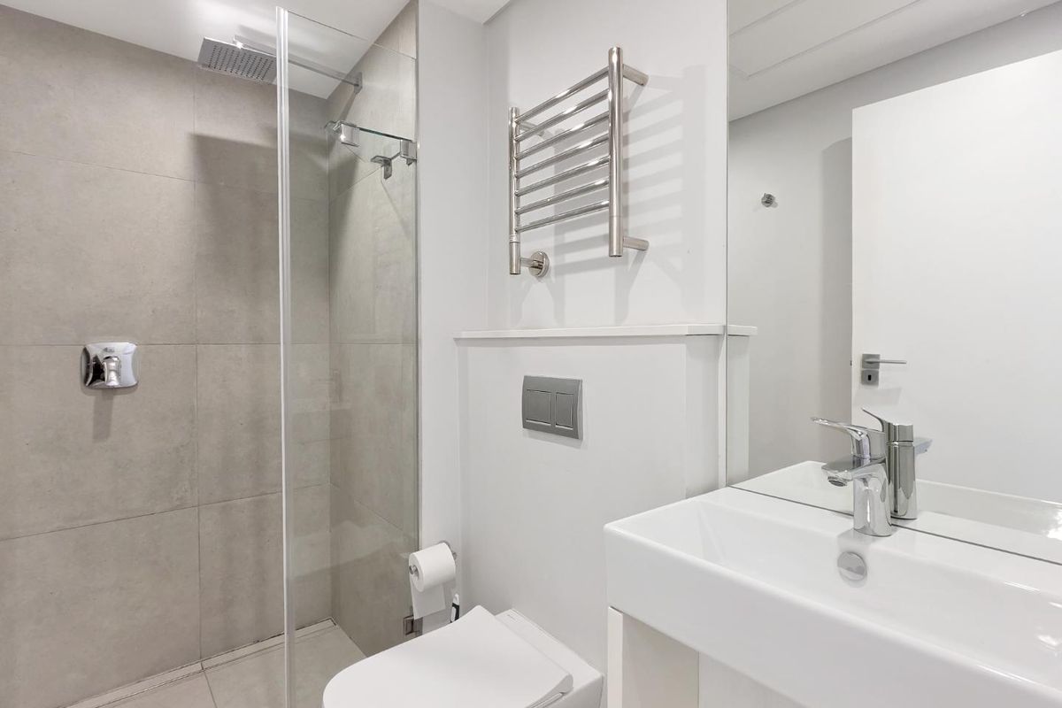 Modern bathroom featuring a walk-in shower with glass screen, wall-mounted toilet, vanity basin, and a chrome heated towel rail.