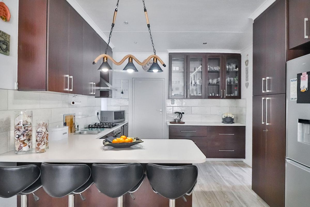 Modern kitchen featuring dark wood cabinetry, stone countertops, a breakfast bar, and integrated stainless steel appliances.