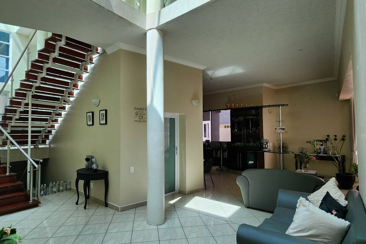Spacious open-plan living area featuring a prominent staircase, tiled flooring, and a built-in bar, illuminated by large windows.