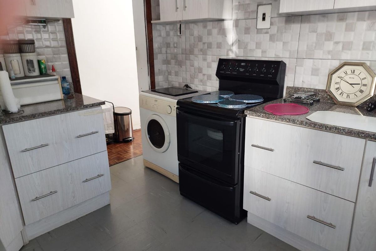Functional kitchen featuring light wood-grain cabinetry, granite countertops, tiled backsplash, and a freestanding stove with an integrated laundry appliance.