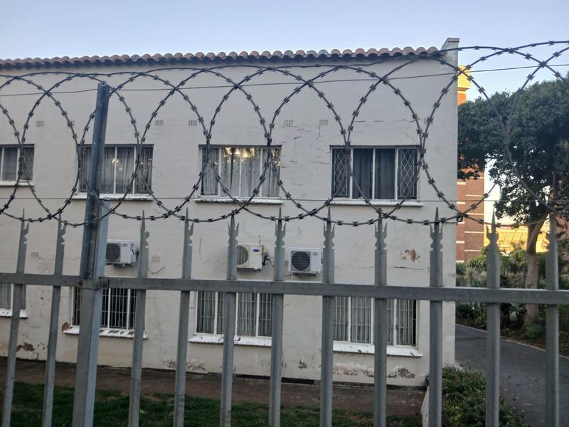 Exterior view of an apartment building facade featuring security fencing with razor wire and multiple wall-mounted air conditioning units.