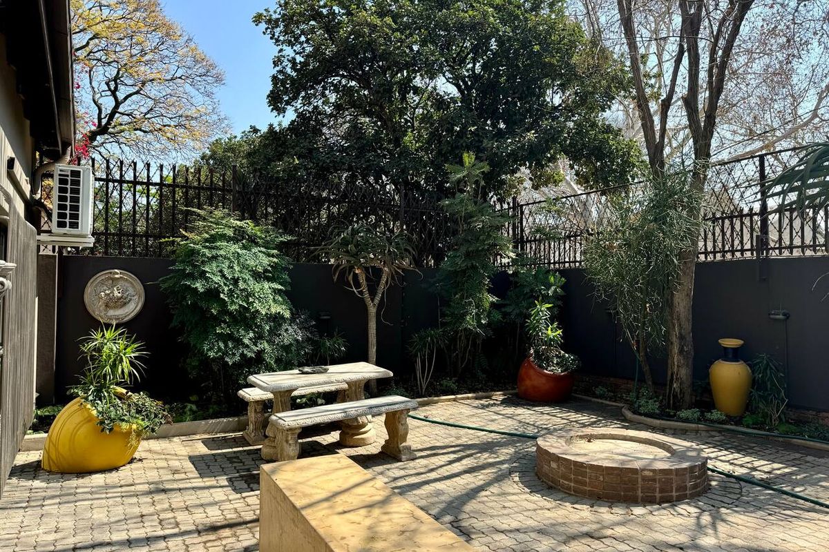 A private rear courtyard featuring paved flooring, a built-in brick fire pit, and perimeter walling with security fencing.