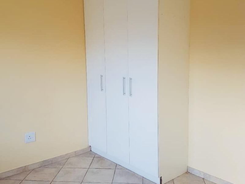 A clean, empty bedroom featuring neutral yellow walls, tiled flooring, and a white built-in wardrobe with modern handles.