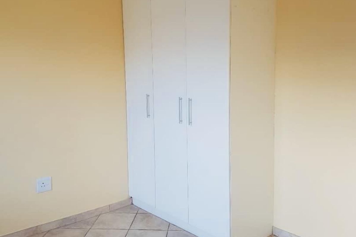 A clean, empty bedroom featuring neutral yellow walls, tiled flooring, and a white built-in wardrobe with modern handles.