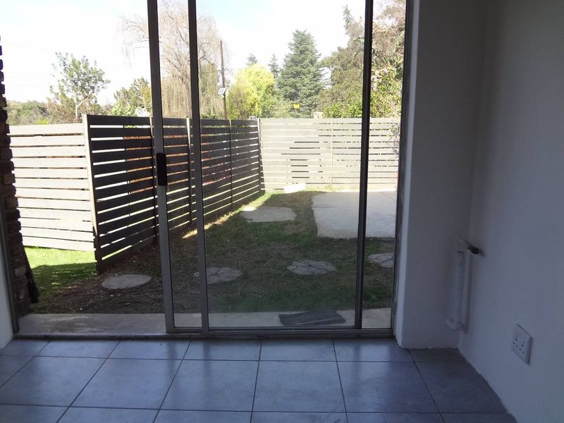 An empty living area featuring ceramic floor tiles and a large sliding glass door providing direct access to a private rear garden with timber fencing.
