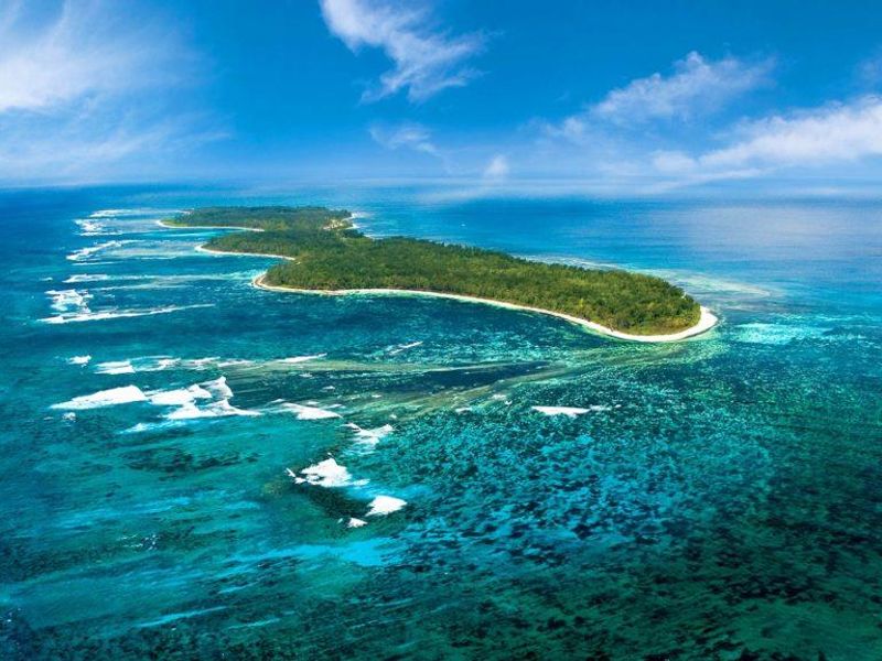An expansive aerial view of a lush tropical island surrounded by vibrant coral reefs and clear blue ocean waters.
