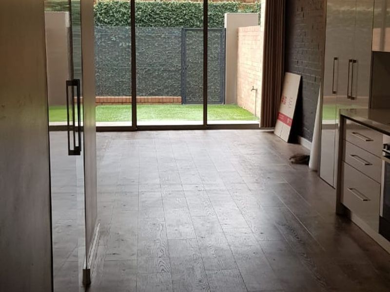 Modern open-plan living area featuring sleek built-in cabinetry, exposed brick accents, and large sliding glass doors opening to a private garden space.