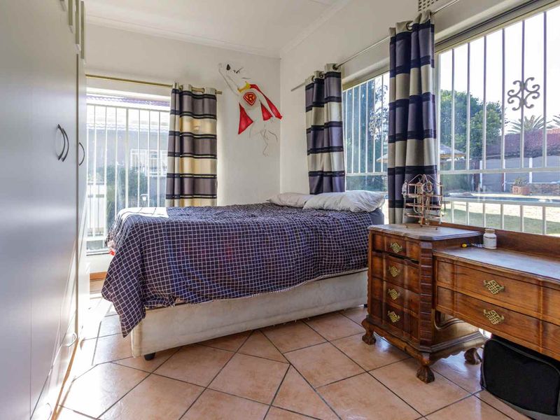 A bedroom featuring tiled flooring, built-in wardrobe storage, and large windows fitted with security bars, offering natural light and views of the garden.