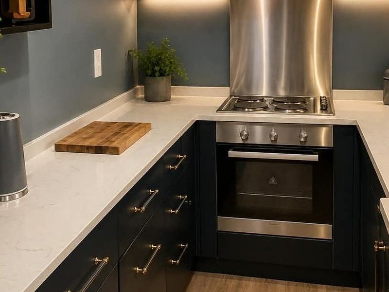 Modern kitchen featuring dark cabinetry, stone countertops, and integrated stainless steel oven and hob with a matching splashback.