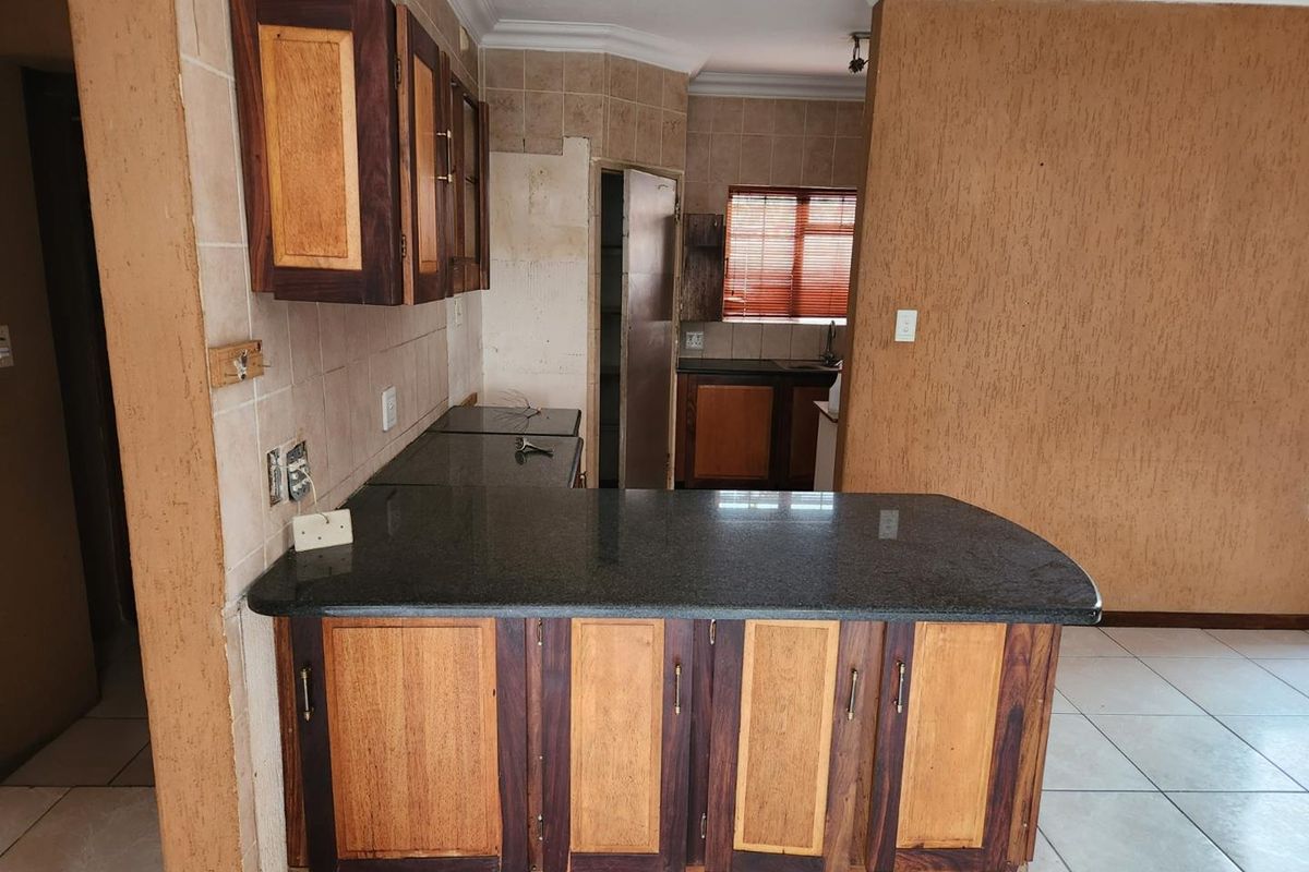 Kitchen area featuring dark granite countertops, wooden cabinetry, and tiled flooring, with an adjacent scullery or prep area visible.