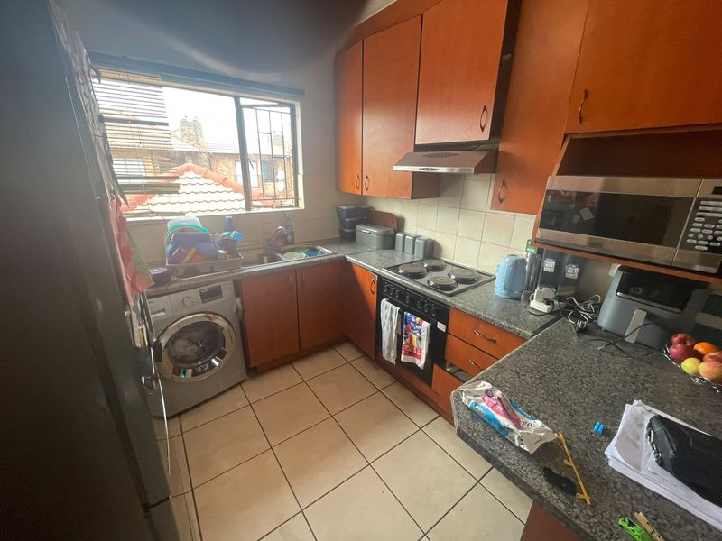 A compact kitchen featuring wooden cabinetry, granite-look countertops, built-in appliances, and tiled flooring, with visible ceiling water damage requiring attention.