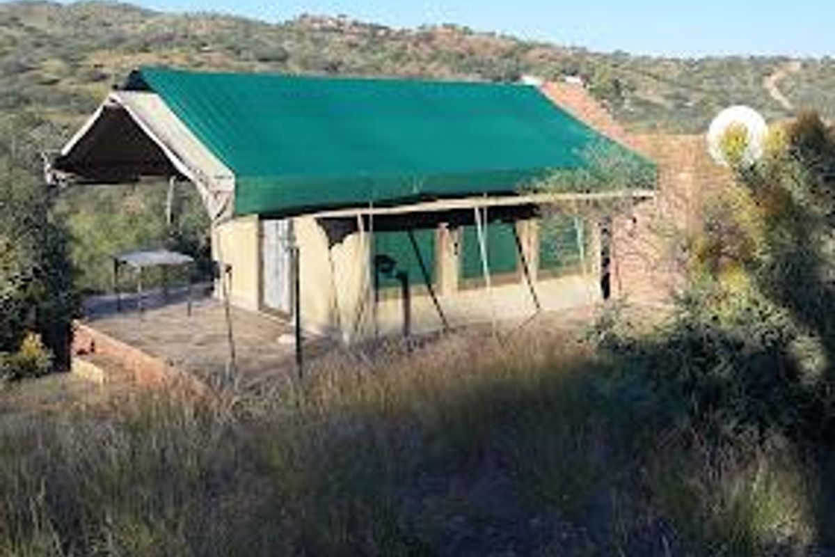 A rustic tented accommodation unit featuring a green canvas roof and a raised platform, set within a natural landscape.
