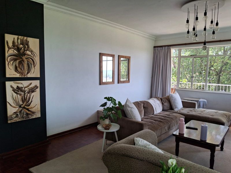 A bright living room featuring classic parquet flooring, decorative cove cornicing, and large windows that provide ample natural light and a pleasant garden view.
