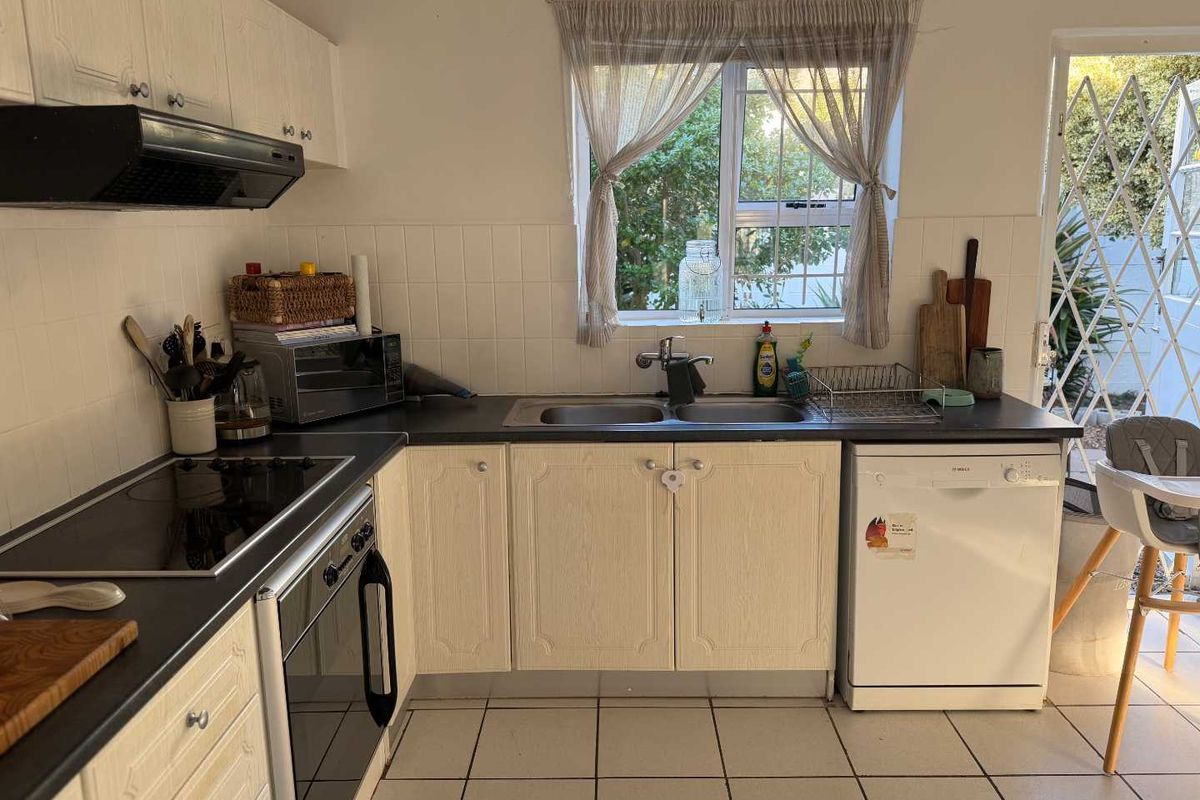 A functional kitchen featuring light-toned cabinetry, dark countertops, a double sink, integrated hob, oven, and extractor fan with tiled flooring.