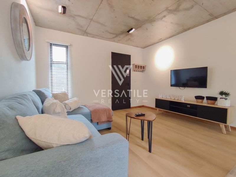 Modern living room featuring an exposed concrete ceiling, light laminate flooring, and recessed lighting, creating a contemporary and industrial-inspired atmosphere.