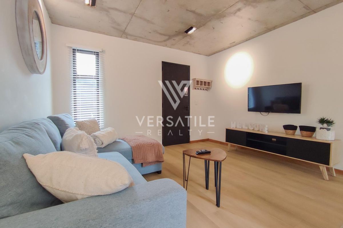 Modern living room featuring an exposed concrete ceiling, light laminate flooring, and recessed lighting, creating a contemporary and industrial-inspired atmosphere.
