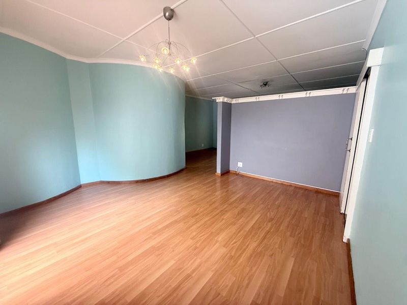 An empty living area featuring laminate flooring, a unique curved wall design, and a suspended ceiling with a modern light fixture.