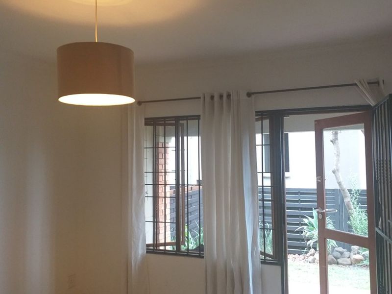 An empty living room featuring tiled flooring, a ceiling rose, and direct access to an outdoor area through a timber door with security bars.