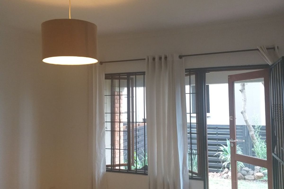 An empty living room featuring tiled flooring, a ceiling rose, and direct access to an outdoor area through a timber door with security bars.