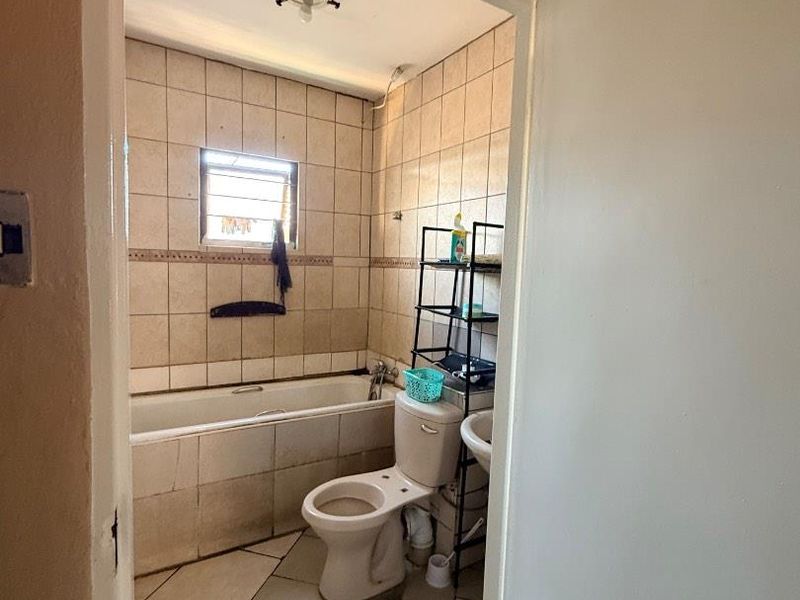 A dated bathroom featuring a bathtub, toilet, and pedestal sink with tiled walls and flooring, requiring cosmetic updates to improve its overall condition.