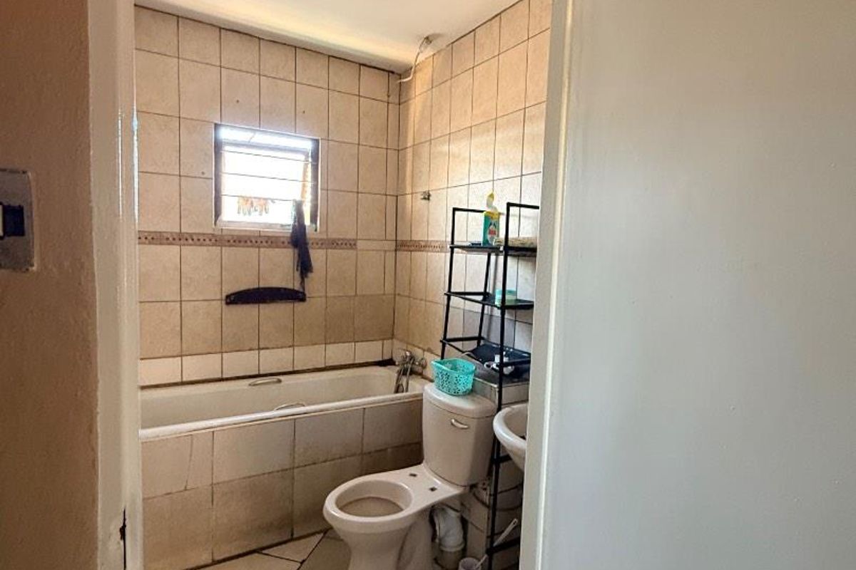 A dated bathroom featuring a bathtub, toilet, and pedestal sink with tiled walls and flooring, requiring cosmetic updates to improve its overall condition.