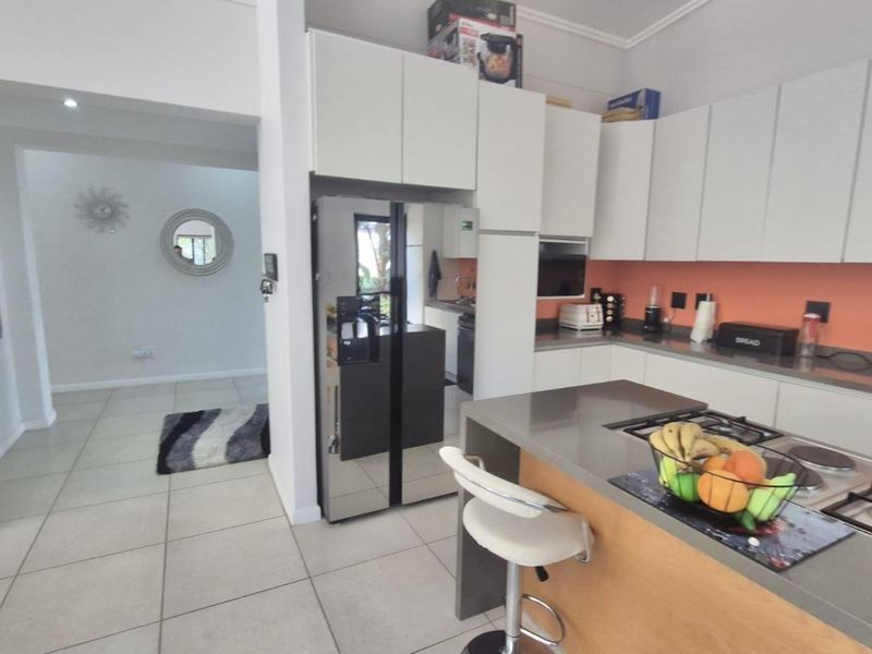 Modern kitchen featuring sleek white cabinetry, stone countertops, a gas hob, and a breakfast bar, seamlessly flowing into the adjacent living area.