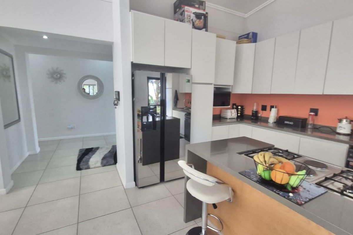 Modern kitchen featuring sleek white cabinetry, stone countertops, a gas hob, and a breakfast bar, seamlessly flowing into the adjacent living area.