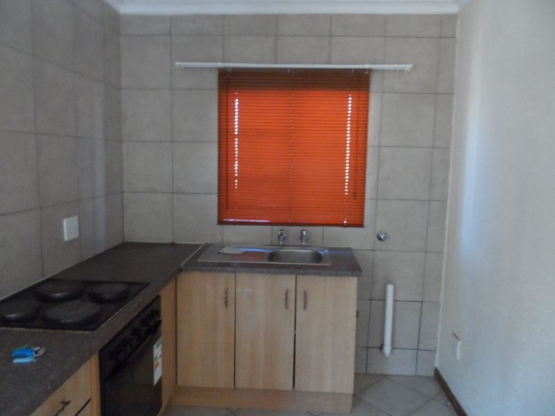 A functional kitchen area featuring built-in cabinetry, a stainless steel sink, an electric hob, and tiled finishes throughout.