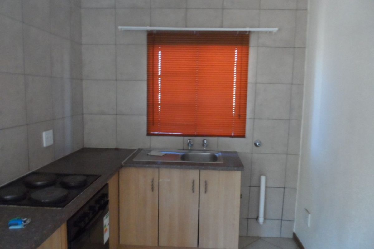 A functional kitchen area featuring built-in cabinetry, a stainless steel sink, an electric hob, and tiled finishes throughout.
