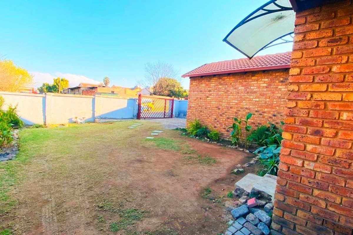 A rear garden area featuring a face brick exterior, boundary wall, and metal gate access, offering potential for landscaping improvements.