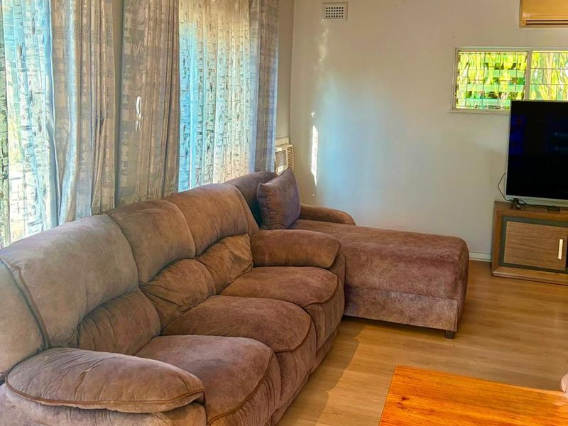 A comfortable living room featuring laminate flooring, recessed downlighting, and a wall-mounted air conditioning unit.