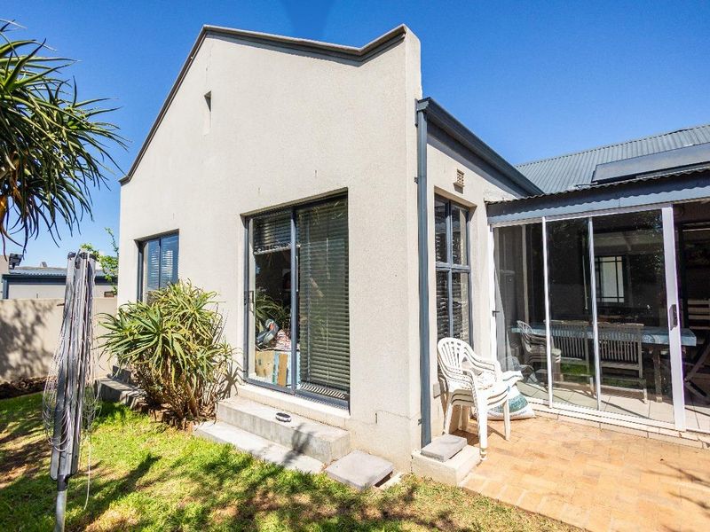 Rear view of the property featuring a paved patio area, sliding glass doors, and a corrugated metal roof with solar water heating.