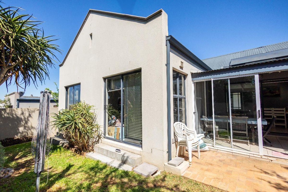 Rear view of the property featuring a paved patio area, sliding glass doors, and a corrugated metal roof with solar water heating.