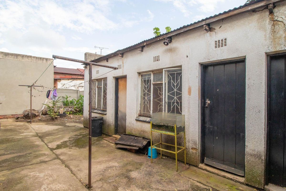 Rear exterior view of the property featuring a concrete courtyard, weathered plaster walls, and multiple access points with security gates.