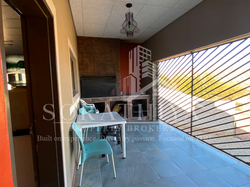 Covered patio area featuring a built-in braai, tiled flooring, and secure metal screening, ideal for outdoor entertaining.