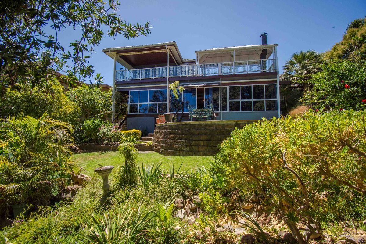 Rear view of a multi-level house featuring a landscaped garden, stone retaining wall, and an elevated balcony with decorative railings.