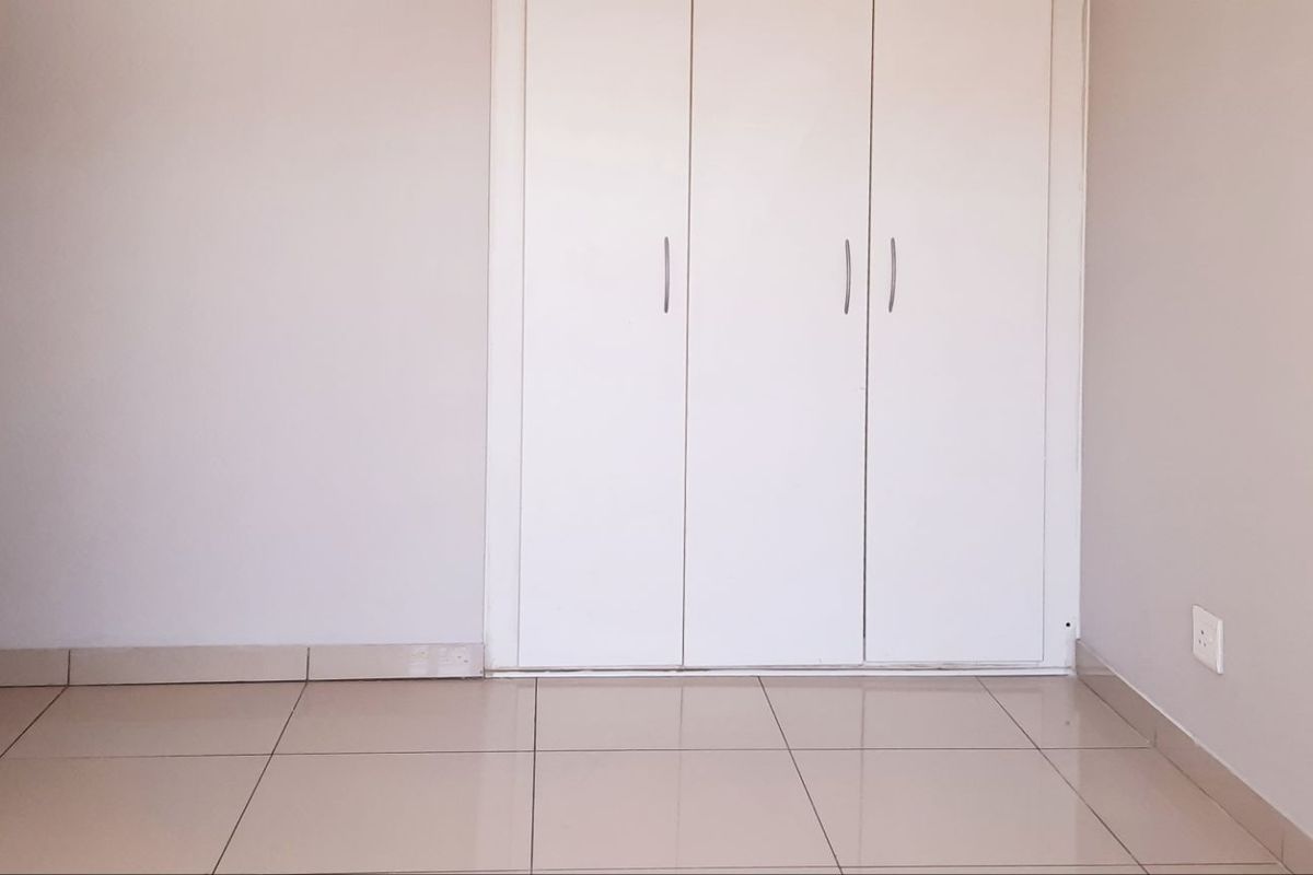 An empty bedroom featuring neutral tiled flooring and white built-in cupboards, providing a clean and versatile space.