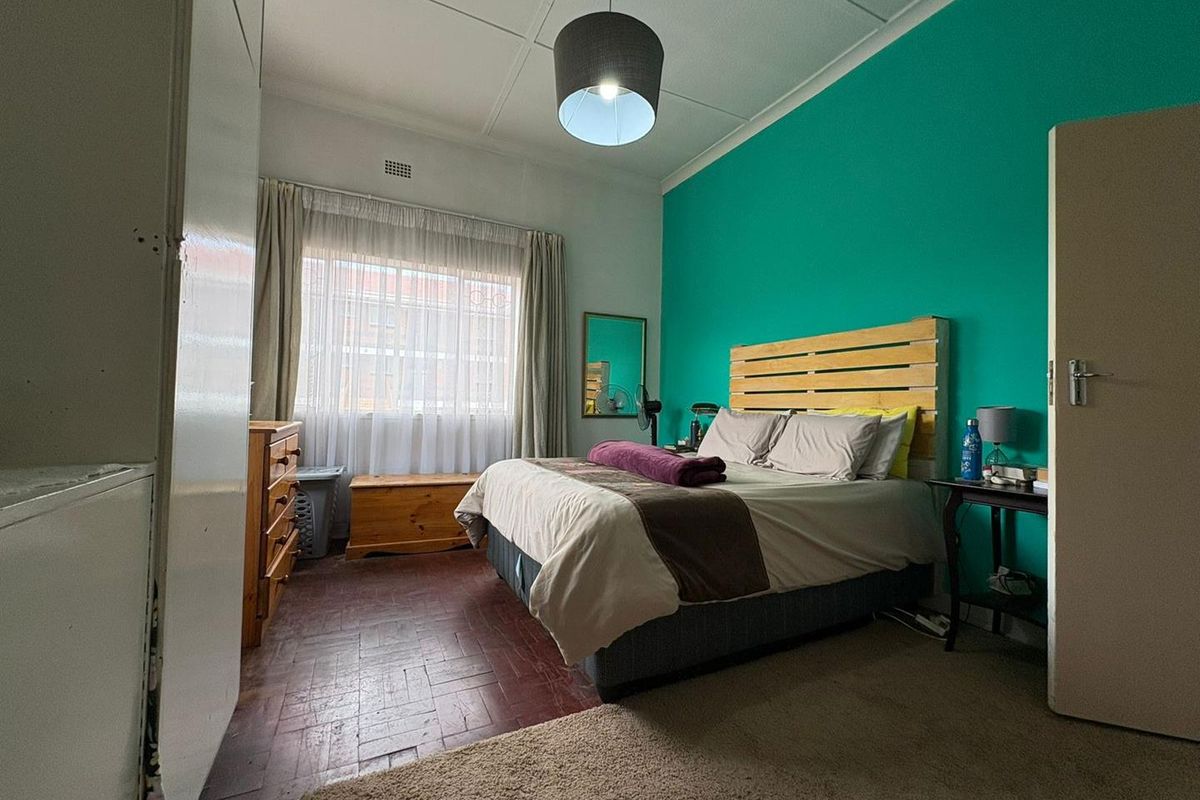 A bedroom featuring parquet flooring, a large window with curtains, and a bold accent wall.
