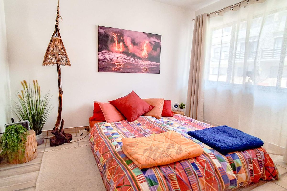 A bright bedroom featuring tiled flooring, neutral walls, and a large window with curtains, providing a comfortable and functional living space.