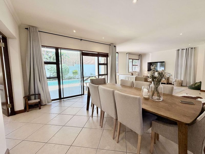 Spacious open-plan living and dining area featuring neutral tiled flooring, recessed lighting, and large sliding glass doors providing seamless access to the outdoor pool area.