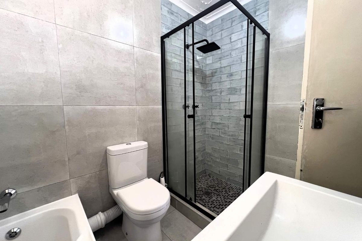 Modern bathroom featuring a glass-enclosed shower with black frame, a white toilet, and large format grey wall tiles.