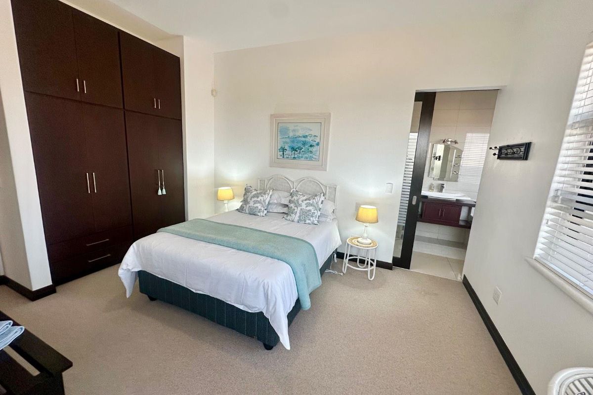 A well-maintained bedroom featuring built-in dark wood cupboards, neutral carpeting, and an adjoining en-suite bathroom with modern fixtures.