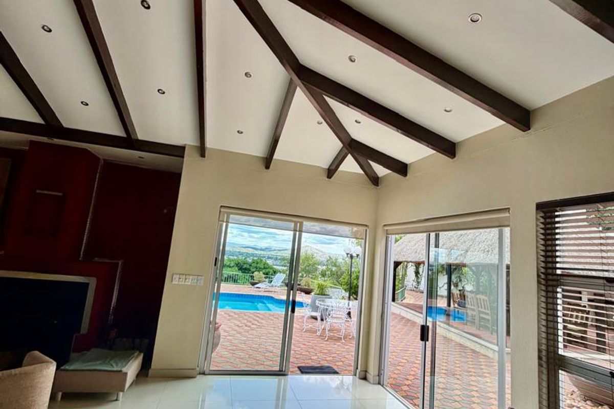 Spacious living area featuring vaulted ceilings with exposed timber beams, large sliding glass doors, and direct access to the outdoor patio and pool area.
