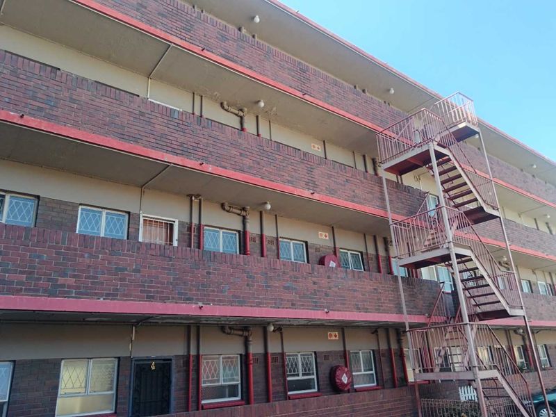 Exterior view of a multi-story brick apartment building featuring an external metal fire escape staircase and security-fitted windows.
